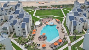 A hotel with a central swimming pool surrounded by lounge areas and umbrellas, adjacent to a beach. - Chic Stay by the Beach (South Padre Island)