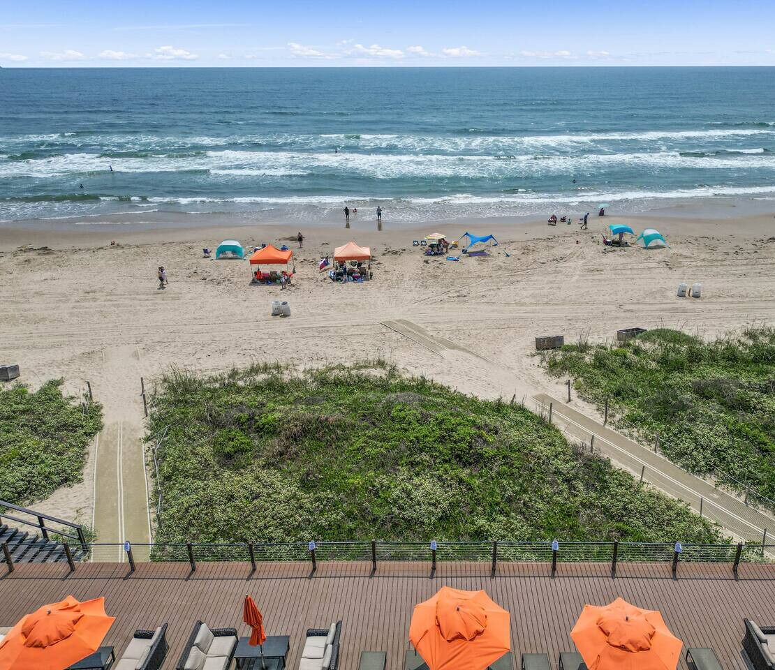 Una playa con sombrillas y sillas de descanso, un camino que lleva a la playa y vistas al océano.