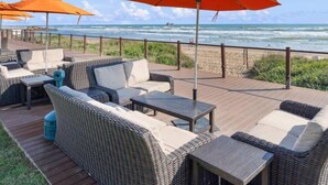 Een terras aan het strand met rieten meubels, oranje parasols en uitzicht op de oceaan.