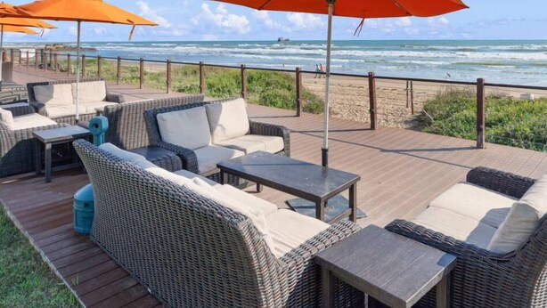 A beachside patio with wicker furniture, orange umbrellas, and a view of the ocean. - Chic Stay by the Beach (South Padre Island)