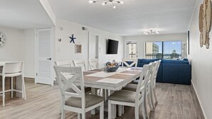 Un comedor moderno con una mesa y sillas blancas, un sofá azul y vistas a la ciudad a través de amplias ventanas.