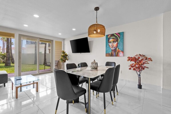 Un comedor moderno con una mesa de mármol, sillas negras y un ventanal con vistas a un jardín.