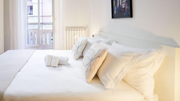 A hotel room with a large bed, white linens, a radiator, a window with curtains, and a framed abstract painting on the wall. - Artists Art Apartment (Torino)