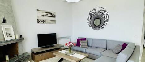 A modern living room with a grey sofa, a flat-screen TV, a coffee table, and a fireplace.