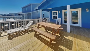 A wooden deck with a picnic table and lounge chairs, overlooking a body of water. - Bayview Cottage by Ryson Vacation Rentals (Galveston)