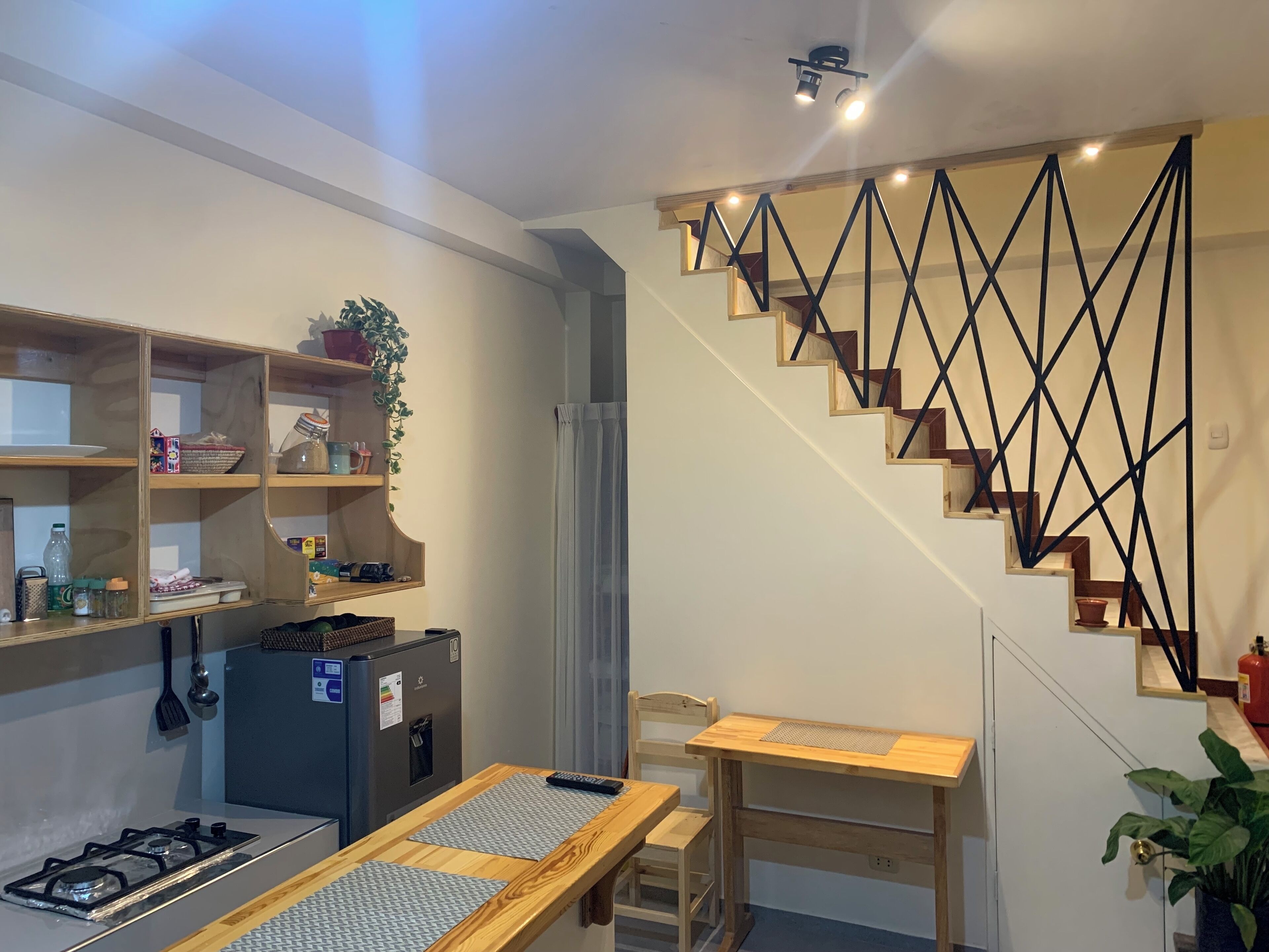 Une cuisine compacte équipée d’une cuisinière à gaz, d’étagères en bois, d’une petite table et d’un escalier doté d’une rampe aux motifs géométriques.