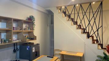 Une cuisine compacte équipée d’une cuisinière à gaz, d’étagères en bois, d’une petite table et d’un escalier doté d’une rampe aux motifs géométriques.