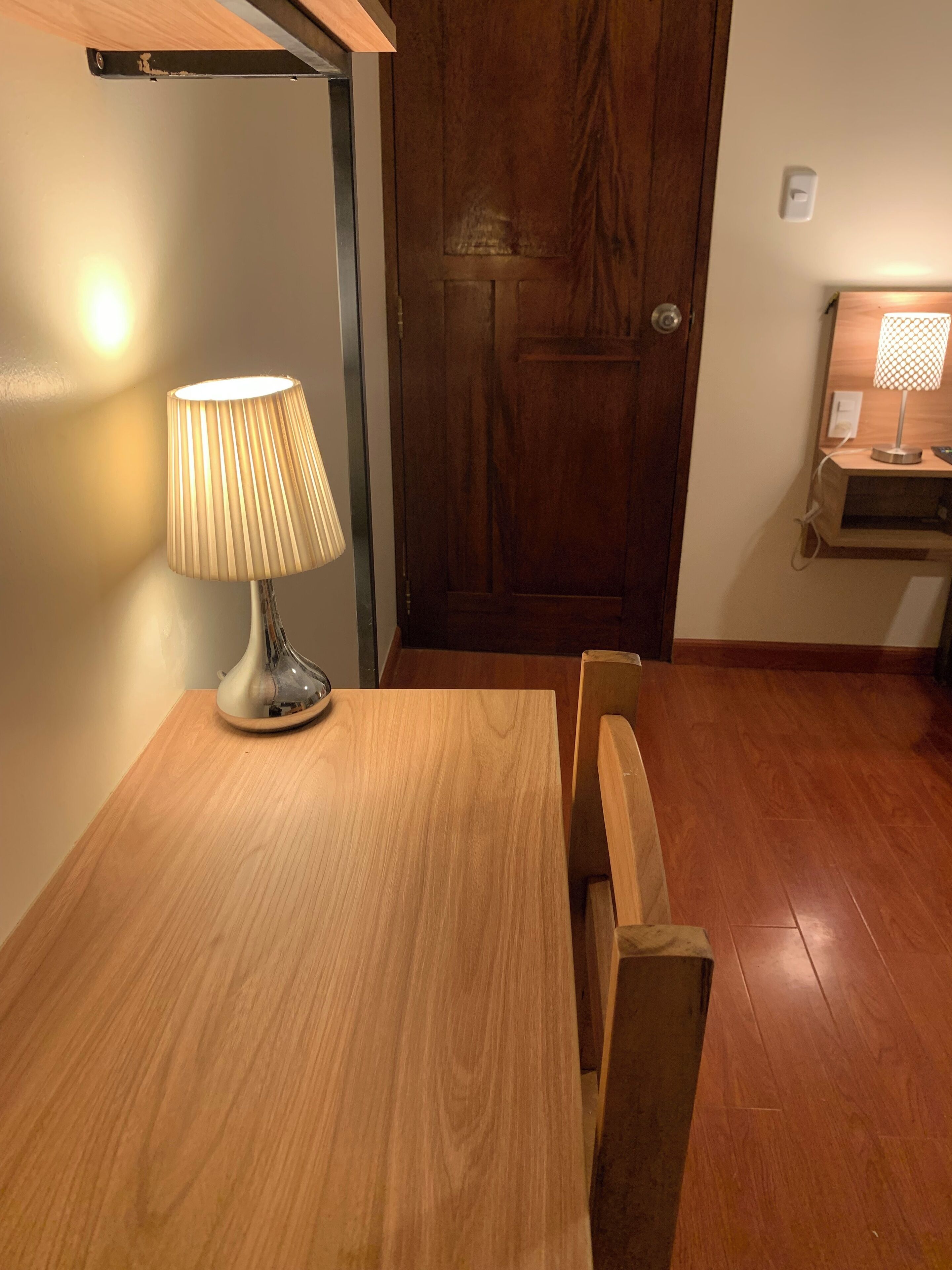 Een houten eettafel met een lamp, een houten deur en een klein plankje met een lamp.