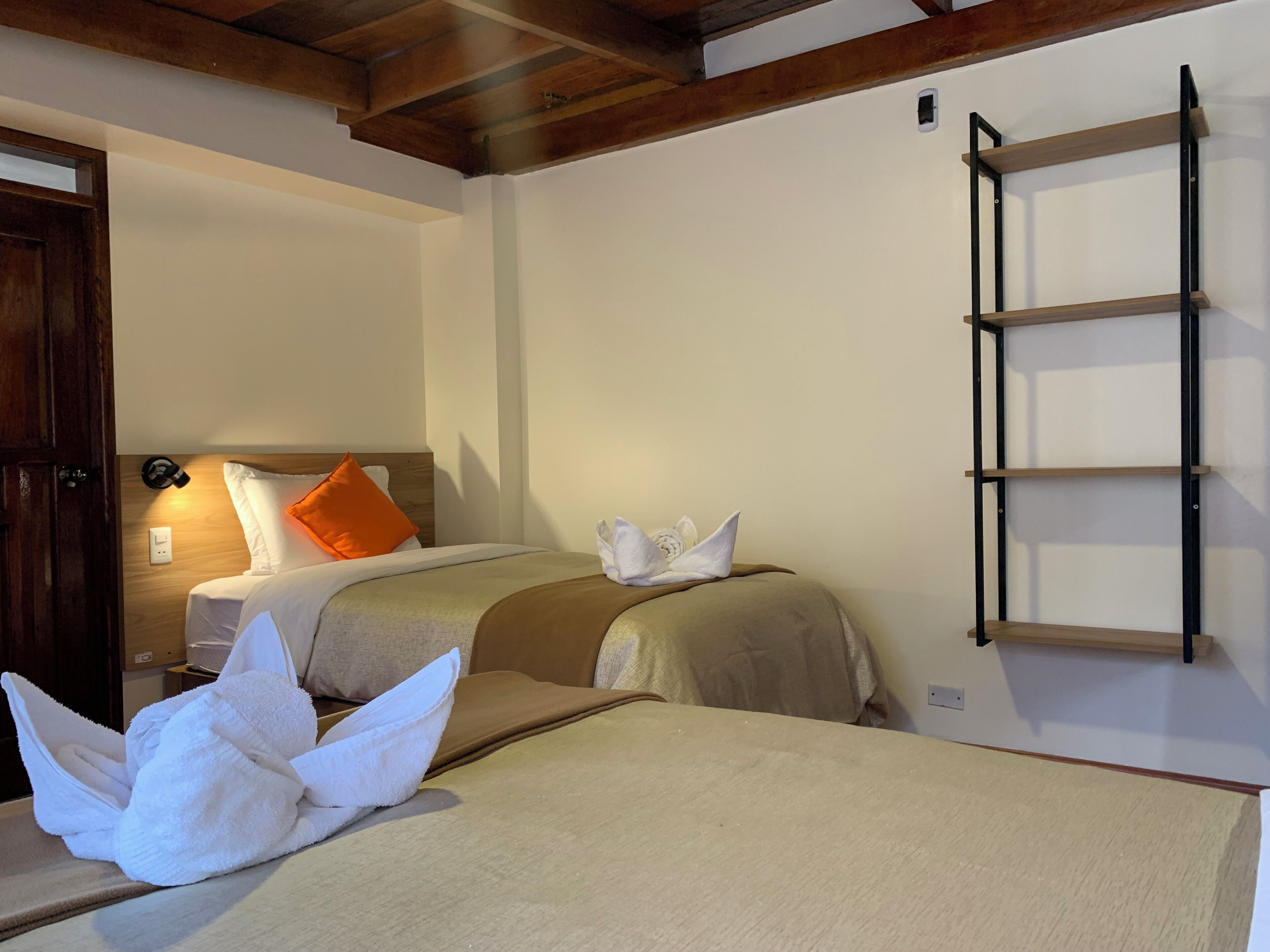 Une chambre d’hôtel avec deux lits, une étagère en bois en forme d’échelle et une porte en bois.