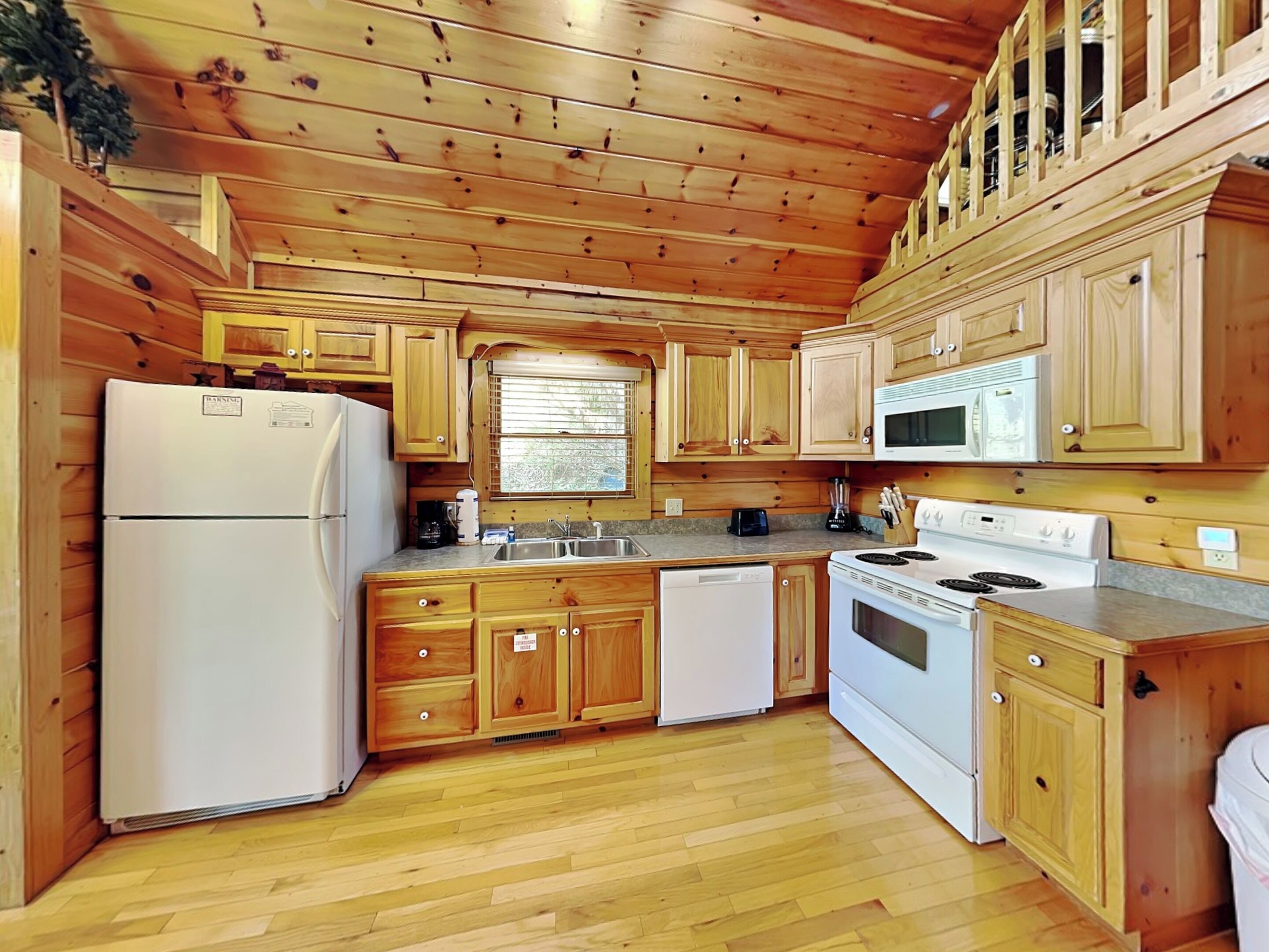 A wooden cabin-style kitchen with a refrigerator, stove, microwave, and wooden cabinets.