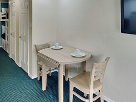 A small dining area with a round table and two chairs, a white cup on the table, and a door with a handle in the background.