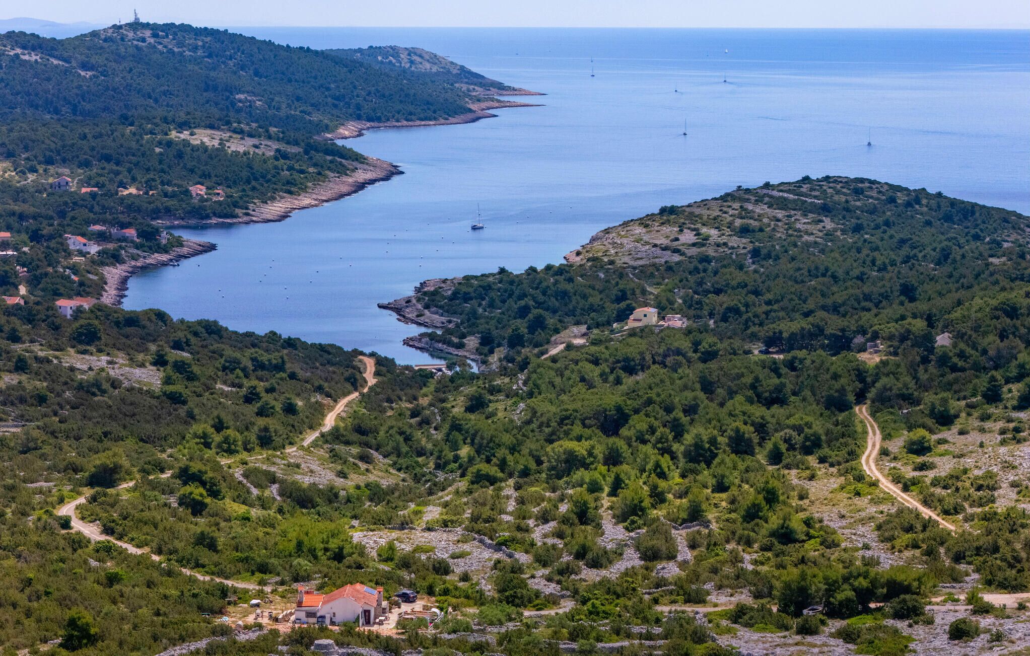 Eine Küstenlandschaft mit einer kurvenreichen Straße, einem kleinen Gebäude mit rotem Dach und freiem Blick auf das Meer.