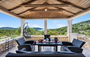 A covered outdoor seating area with wicker furniture, a hanging chair, and a table set with a fruit bowl and glasses. - Gorgeous home in Zirje with WiFi (Zirje)