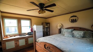 A bedroom with a wooden bed, a ceiling fan, a refrigerator, a microwave, and a window with a view.