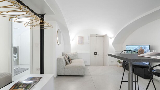 A modern, minimalist living space with a grey sofa, a dining table, and a kitchen area. - Torino | Gioia House (Torino)