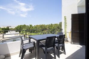 A balcony with a table and chairs, a potted plant, and a view of a building and trees.