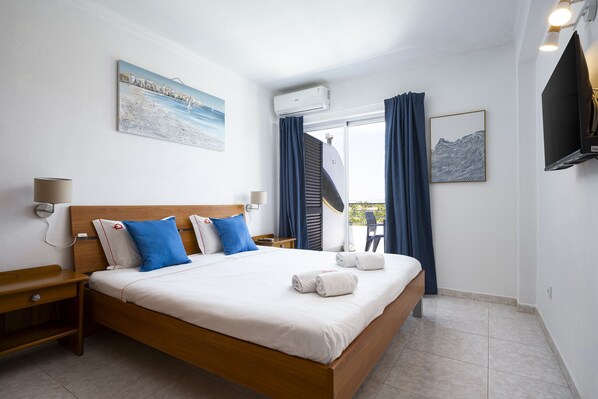 A hotel room with a bed, a nightstand, a wall-mounted TV, and a window with curtains.