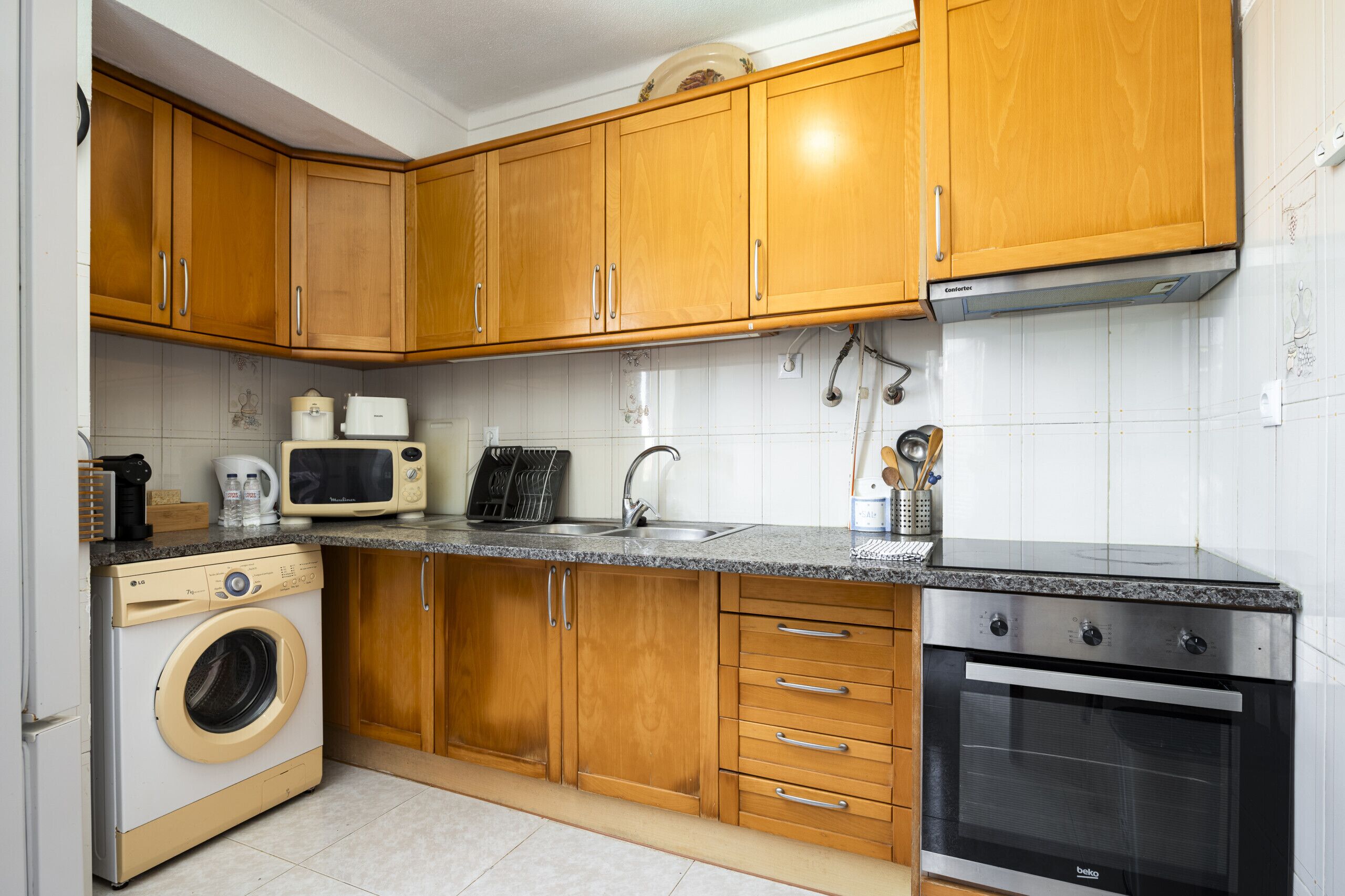 A kitchen with wooden cabinets, a washing machine, a microwave, a sink, and an oven.