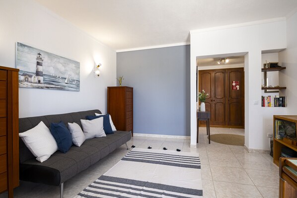 A living room with a grey sofa, wooden cabinet, and a painting of a lighthouse.