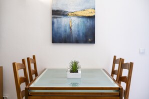 Una mesa de comedor con tapa de vidrio, rodeada de sillas de madera y una pequeña planta en maceta sobre la mesa.