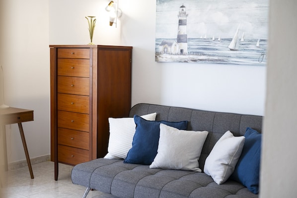 Ein Zimmer mit grauem Sofa, einem Holzschrank und einem Gemälde eines Leuchtturms.