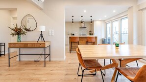 A modern kitchen with wooden cabinets, a dining area with a wooden table and chairs, and a large window providing natural light.