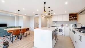 A modern kitchen with a central island, built-in oven, and a dining area with a wooden table and chairs.