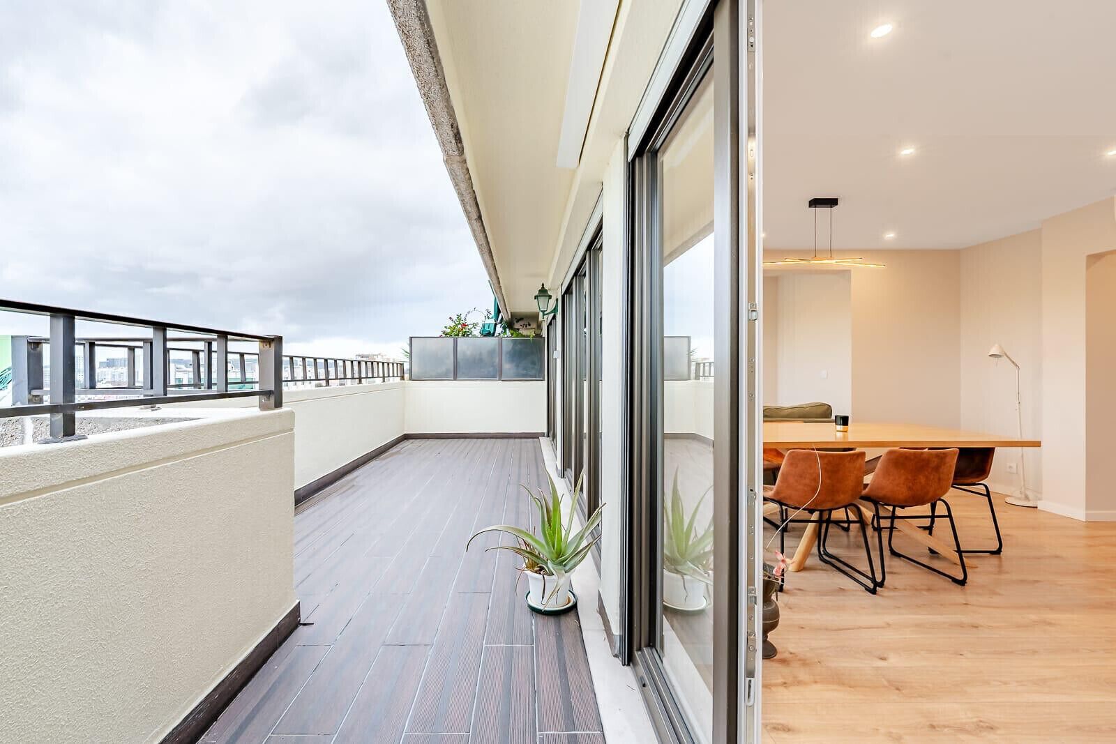 A modern apartment with a balcony, a dining area with a wooden table and chairs, and a view of the cityscape.