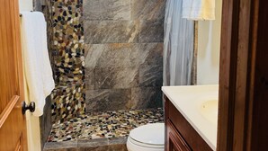Un baño con pared de ducha de piedra, inodoro y muebles de madera.
