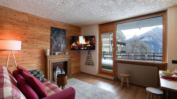 Un salon chaleureux avec une cheminée, un téléviseur et une grande fenêtre donnant sur les montagnes.