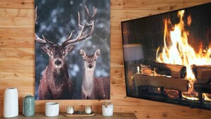 Un mur en bois orné d’un tableau représentant un cerf, encadré, et d’un téléviseur diffusant une image de feu de cheminée.