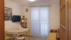A small, well-lit room with a dining table, chairs, a TV, a bookshelf, and a sofa. - Apartment Spajic by aneo travel (Klek)
