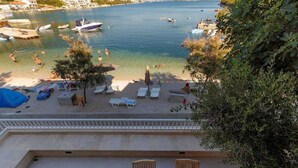 A beach with clear water, lounge chairs, and umbrellas. Boats are visible in the water. - Apartment Spajic by aneo travel (Klek)