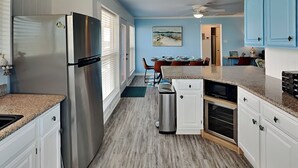 A modern kitchen with white cabinets, a stainless steel refrigerator, and a dining area with a table and chairs. - Once Upon a Tide by Ryson Vacation Rentals (Galveston)
