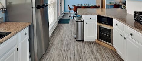 A modern kitchen with white cabinets, a stainless steel refrigerator, and a dining area with a table and chairs.