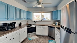 A kitchen with blue cabinets, stainless steel appliances, and a window with a view. - Once Upon a Tide by Ryson Vacation Rentals (Galveston)