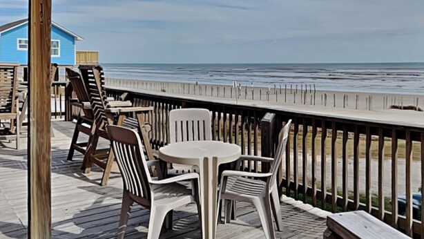 A wooden deck with outdoor furniture overlooking a beach. - Once Upon a Tide by Ryson Vacation Rentals (Galveston)