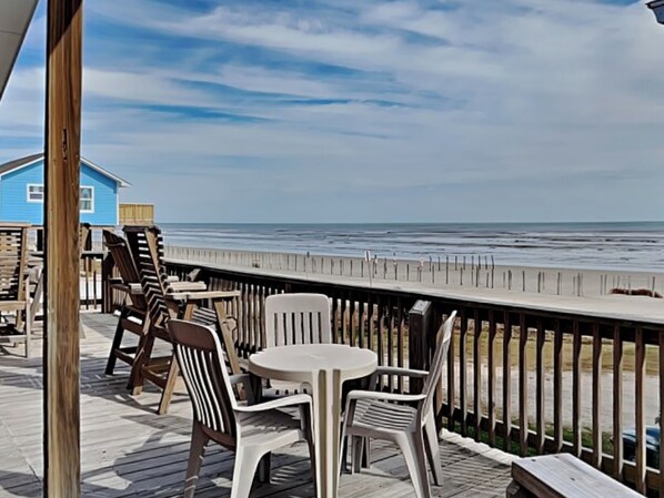 A wooden deck with outdoor furniture overlooking a beach. - Once Upon a Tide by Ryson Vacation Rentals (Galveston)
