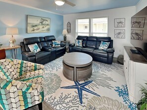 A living room with two black leather sofas, a round coffee table, and a patterned rug. - Once Upon a Tide by Ryson Vacation Rentals (Galveston)