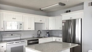A modern kitchen with white cabinetry, stainless steel appliances, and a granite countertop island.