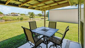An outdoor patio with a table and chairs, a covered area, and a view of a grassy field and distant buildings. - Sorry Charlie's by Miss Kitty’s (Rockport)