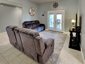 A living room with a sectional sofa, a rug, a wall clock, a door leading to a balcony, and a TV stand. - Sorry Charlie's by Miss Kitty’s (Rockport)