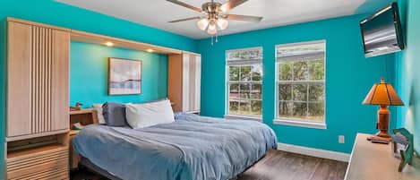Un dormitorio con una cama, ventilador de techo, ventana y televisor.