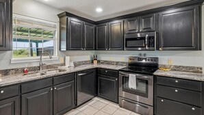 A kitchen with dark cabinets, a stainless steel stove, a microwave, and a window with a view. - Sorry Charlie's by Miss Kitty’s (Rockport)