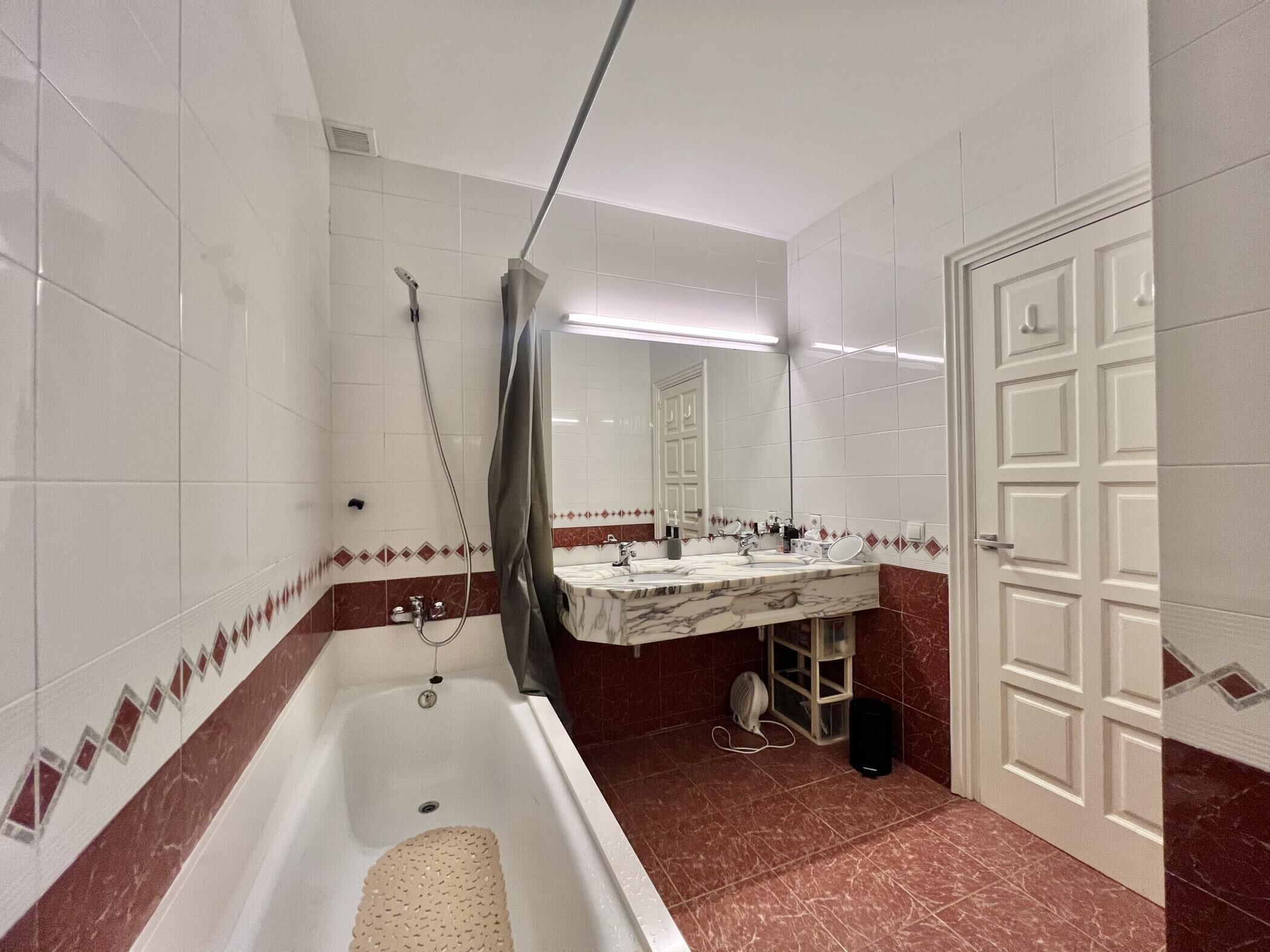 A bathroom with a bathtub, a shower, a sink with a mirror, and a door.