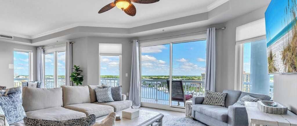 A spacious living room with a large sofa, a smaller couch, and a coffee table. There is a balcony with a view of the city.