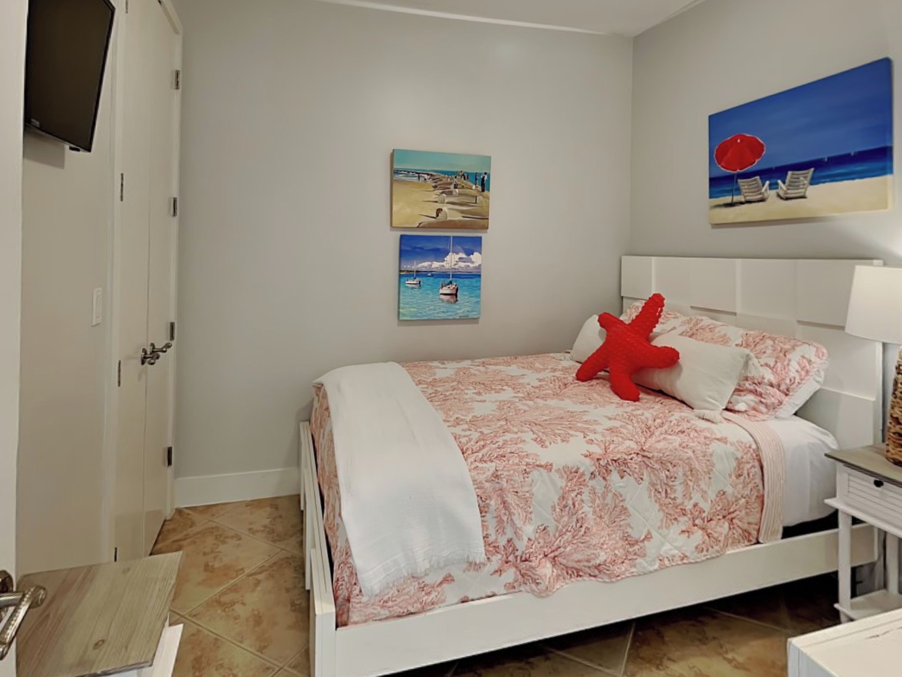 A bedroom with a bed, a red starfish pillow, and two paintings on the wall.