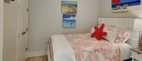 A bedroom with a bed, a red starfish pillow, and two paintings on the wall.