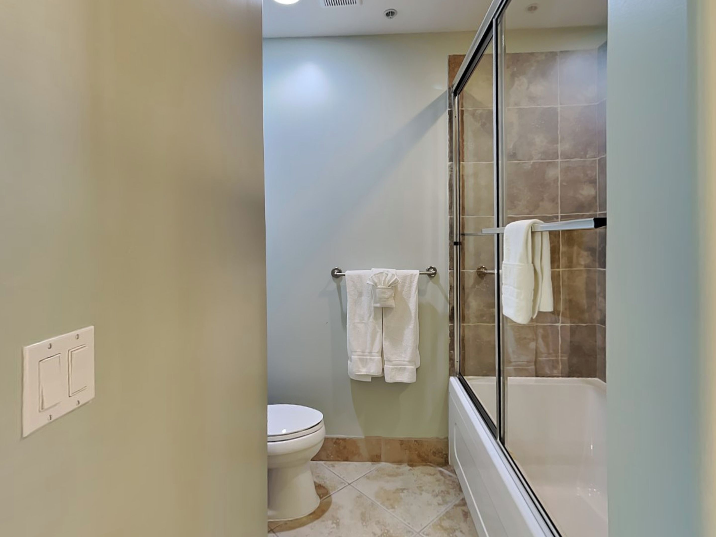 A bathroom with a toilet, a glass-enclosed shower, and a towel rack with multiple towels.