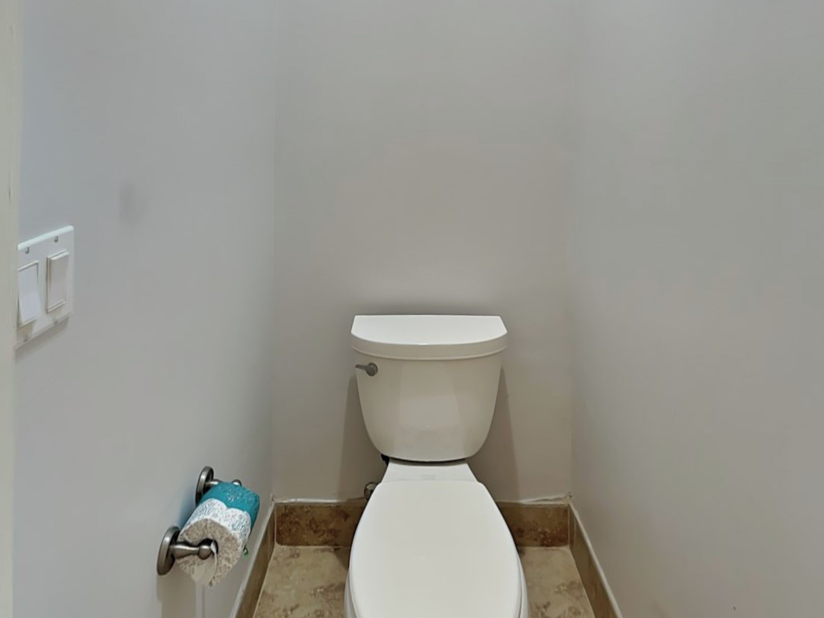 Um banheiro pequeno e limpo, com vaso sanitário branco, porta-toalhas e uma toalha azul e branca, e uma parede lisa.